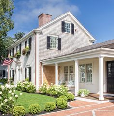 a white house with black shutters and flowers in the front yard