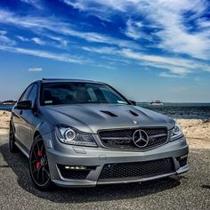 a silver car parked on top of a parking lot next to the ocean in front of a blue sky