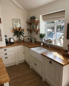 a kitchen with white cabinets and wooden counter tops, sunflowers on the window sill