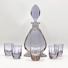 a glass decanter with four glasses in front of it on a white background