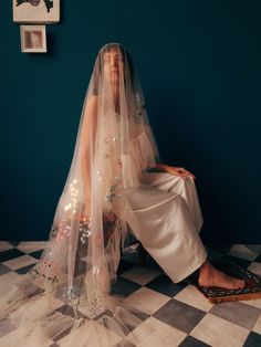 a woman sitting on top of a checkered floor next to a wall wearing a veil