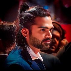 a man with long hair wearing a suit and tie in front of other people at an event