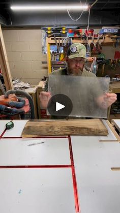 a man holding up a piece of wood in front of a table with tools on it