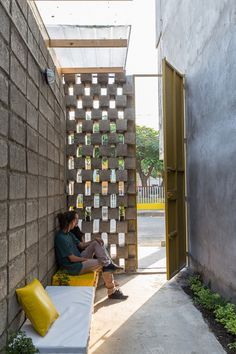 a person sitting on a bench with a laptop in front of a wall that is made out of bottles