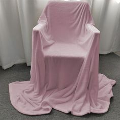 a chair covered in a pink blanket sitting on top of a gray floor next to a window