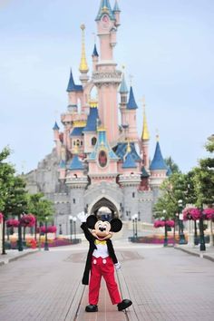 a man in mickey mouse costume standing on the side of a road with a castle behind him