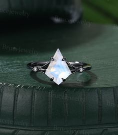 an engagement ring with a faceted white stone in the center on top of a green surface