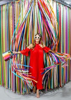 a woman in a red dress and sunglasses standing next to a colorful wall with streamers