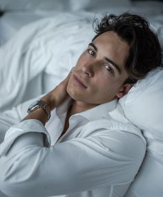 a man laying in bed with his hands on his head and looking at the camera