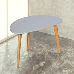 an oval table with two wooden legs and a gray top sits in front of a white wall