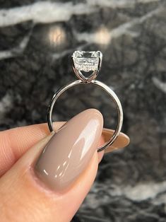 a woman's hand holding a ring with a diamond on it, in front of a marble background