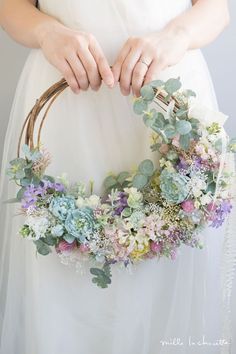 a woman holding a wreath with succulents and greenery in her hands