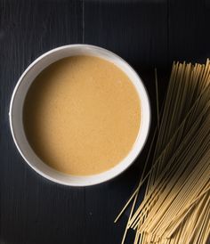 a white bowl filled with noodles next to a wooden spoon on top of a table