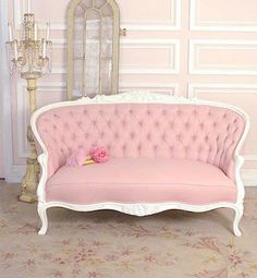 a pink couch sitting in front of a white wall next to a chandelier