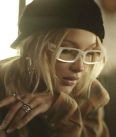 a close up of a person wearing glasses and a hat with rings on her finger