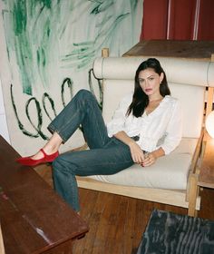 a woman sitting in a chair with her legs crossed on the floor and wearing red shoes