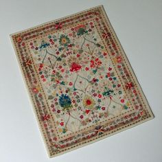 a square rug with flowers on it sitting on top of a white table next to a wall