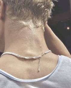 the back of a woman's neck wearing a silver chain necklace with a cross on it