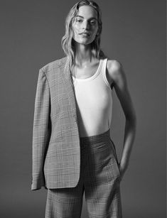 a woman is standing in front of a gray background wearing a white tank top and plaid pants