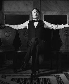 a man in a tuxedo sitting on a chair with his arms spread out