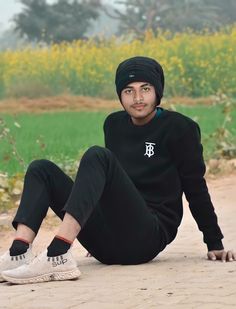 a man sitting on the ground with his legs crossed wearing a black hat and sweatpants