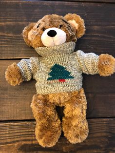 a brown teddy bear wearing a sweater with a christmas tree on it's chest