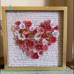 a heart made out of paper flowers sitting on top of a piece of paper with the word love spelled in it