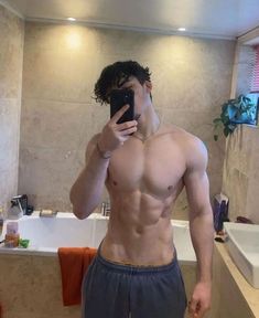 a shirtless man taking a selfie in front of a bathroom mirror with his cell phone