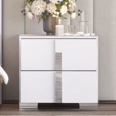 a white dresser with flowers and candles on it next to a chair in a room