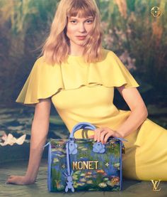 a woman sitting on the ground with a handbag in front of her, wearing a yellow dress