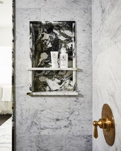 a bathroom with marble walls and shelves on the wall, along with a gold faucet