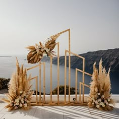 an arrangement of flowers and feathers on display in front of a mountain range with water