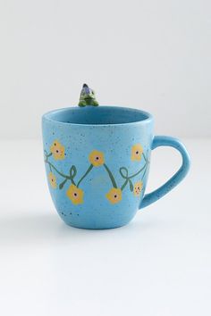 a blue coffee cup with yellow flowers painted on the outside and inside, sitting on a white surface