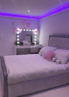 a white bed sitting in a bedroom next to a dresser and mirror with lights on it