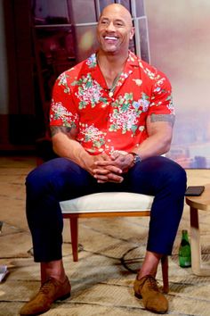 a man sitting on top of a white chair in front of a tv screen wearing a red shirt and blue pants