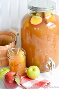 a jar filled with orange juice next to apples