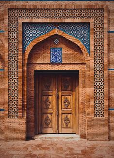 two wooden doors in front of a brick building with blue and white designs on it