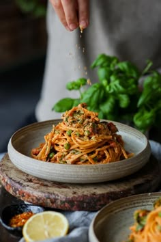 someone sprinkling parmesan cheese on top of spaghetti