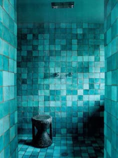 a blue tiled room with a stool in the corner and tile on the wall behind it