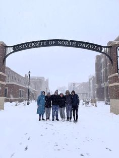 four people standing under an arch on a snowy day in front of the university of north dakota