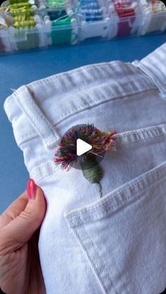 someone is holding out their white jeans with a flower in the pocket and thread spools sticking out of it