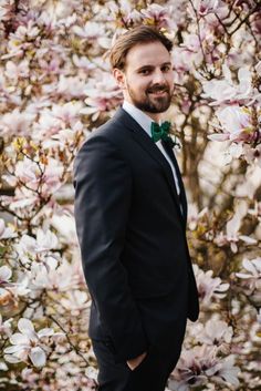 a man wearing a suit and bow tie standing in front of a tree with pink flowers