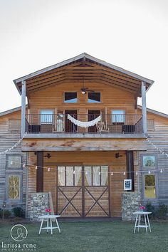 a large wooden house with a hammock hanging from the roof and two white chairs in front of it