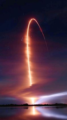 a long exposure shot of a rocket taking off into the night sky with its reflection in the water