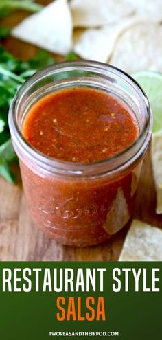 a jar filled with salsa sitting on top of a wooden table next to tortilla chips