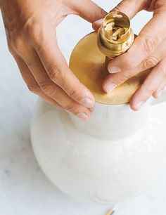 two hands holding a gold ring over a white container