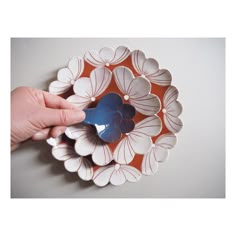 a hand is holding a blue and white flower shaped dish on an orange plate with leaves