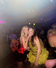 two women dressed in bee costumes pose for the camera at a party with other people