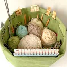 a green basket filled with yarn and knitting needles