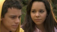 a young man and woman in yellow hoodies looking at something on the ground with trees in the background